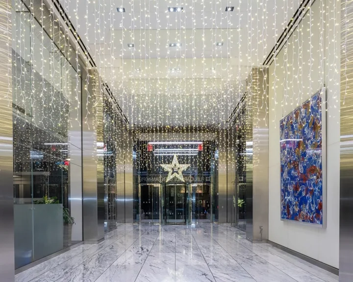 Rows of hanging white lights and an illuminated star in a marble-floored lobby corridor