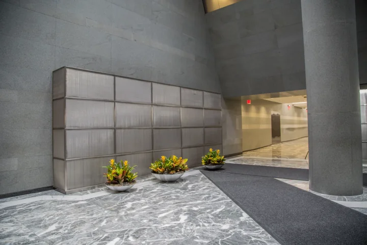 Low bowl planters with colorful foliage beside a paneled wall in a stone-floored lobby