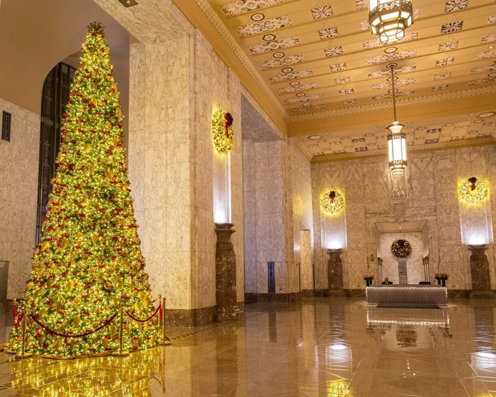 Tall illuminated tree with gold ornaments and wall wreaths in a spacious stone lobby