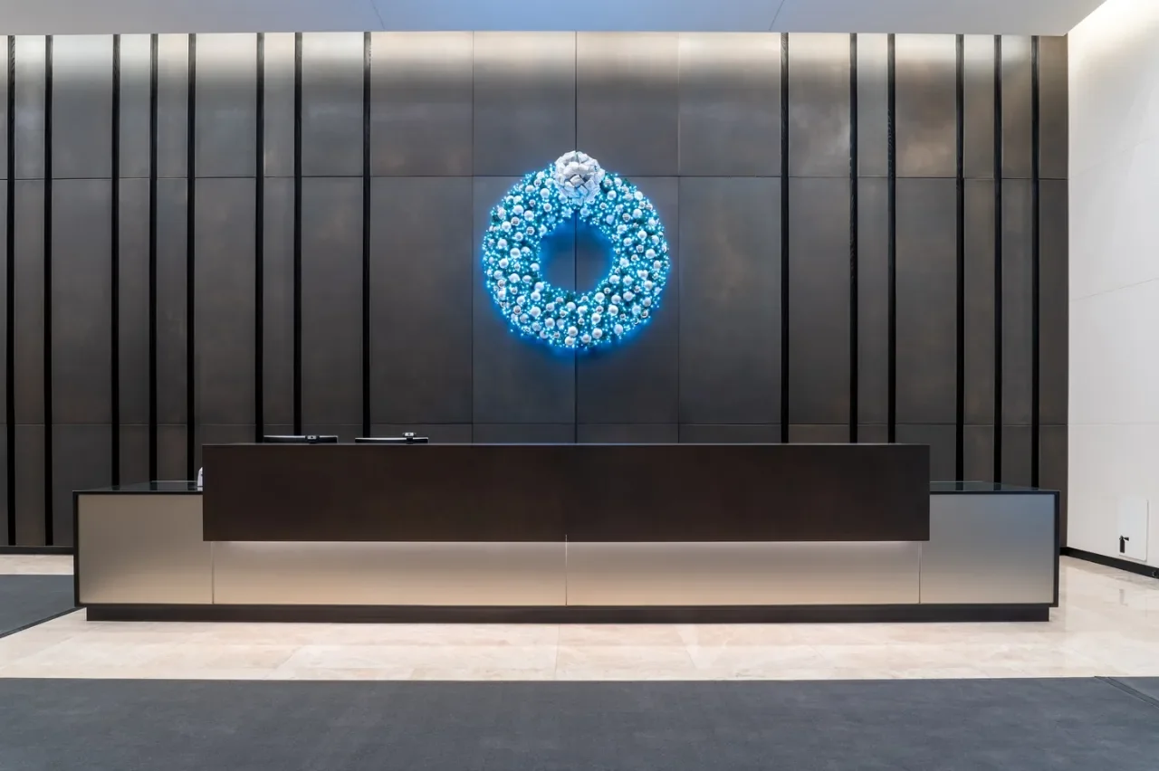 An illuminated blue wreath above a reception counter against a dark paneled wall